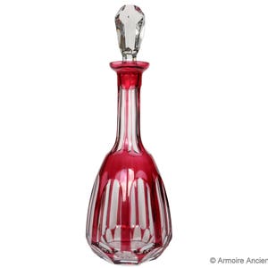 May include: A red and clear glass decanter with a faceted stopper. The decanter has a ribbed design.