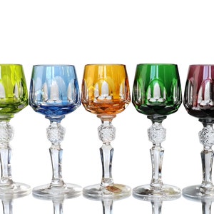 Könnte beinhalten: Fünf Kristallgläser mit Stiel und geschnittenen Mustern. Die Gläser sind in verschiedenen Farben: grün, blau, orange, grün und lila.