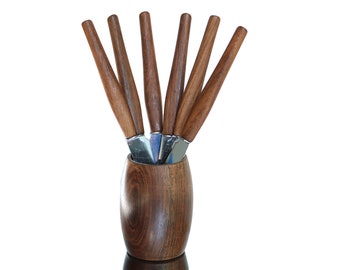 May include: A set of six wooden handled knives with silver blades are displayed in a wooden holder. The holder is a dark brown color and has a rounded shape.