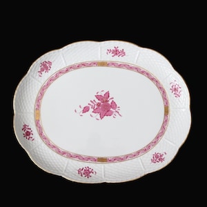 Op de afbeelding: Witte ovale serveerschaal met een roze bloemenmotief en gouden rand. De schaal heeft een reliëf, getextureerd oppervlak.