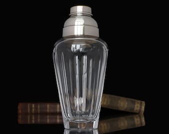 May include: A clear glass cocktail shaker with a silver top. The shaker has a fluted design and a round base.