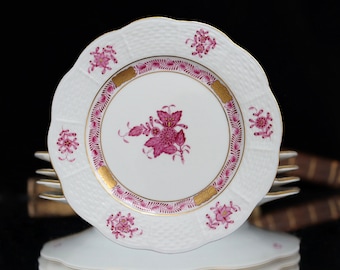 May include: A set of white porcelain plates with a pink floral design and gold trim. The plates have a scalloped edge and a raised, textured surface.