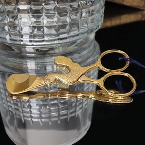 Puede incluir: Separador de huevos de metal dorado en forma de pollo con una cinta azul. El separador tiene una cuchara y un par de tijeras.