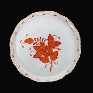 May include: White ceramic plate with a scalloped edge, featuring a floral design in shades of orange and red. The rim is accented with a gold and red geometric pattern. A decorative piece for serving.