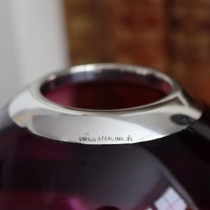 Peut inclure: Gros plan sur un vase en verre violet fonc&eacute; avec un bord argent&eacute;. Le vase a une forme arrondie et une surface lisse et brillante. Le texte "925 STERLING" est estampill&eacute; sur le bord argent&eacute;.