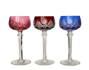 May include: Three stemmed wine glasses with intricate cut glass designs. The glasses are red, blue, and clear.