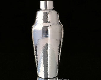 Puede incluir: Un coctelera de plata con acabado martillado. La coctelera tiene un cuerpo redondeado y un diseño clásico.