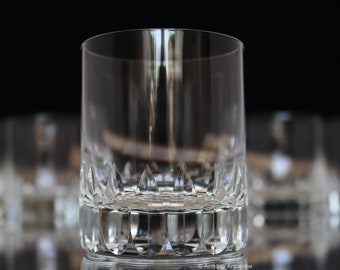 May include: A clear, cut-crystal tumbler with a thick base and a straight, cylindrical shape. The bottom of the glass features a series of pointed, triangular cuts. The glass is designed to hold liquids and is suitable for serving beverages.