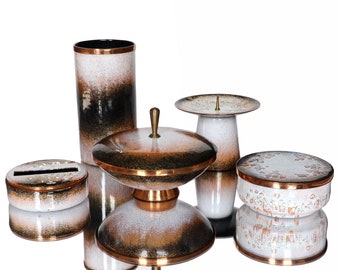 May include: Set of five white and copper colored ceramic decorative items. The items include a tall cylinder vase, a round bowl with a lid, a small round box, a round pedestal with a small plate on top, and a round box with a lid. The items are all decorated with a white and copper speckled pattern.