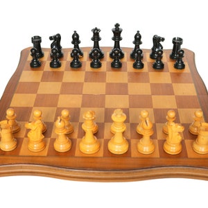 Peut inclure: Un échiquier en bois avec des cases noires et blanches. Les pièces d'échecs sont disposées pour le début d'une partie. Les pièces blanches sont en bois et les pièces noires sont en plastique noir.