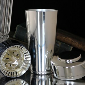 K&ouml;nnte beinhalten: Ein silberner Cocktailshaker mit einem Sieb und einem Deckel. Der Shaker ist aus Metall und hat eine gl&auml;nzende Oberfl&auml;che.