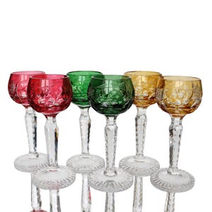 Puede incluir: Conjunto de seis copas de vino con tallo en varios colores: rojo, verde y amarillo. Cada copa presenta un diseño decorativo grabado en el cuenco y un tallo transparente facetado. Las copas están dispuestas sobre un fondo blanco.