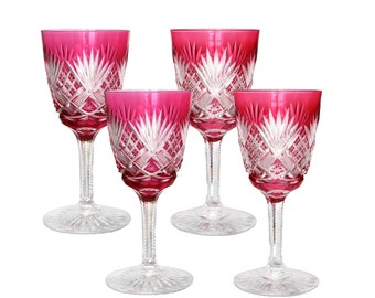 May include: Set of four ruby red wine glasses with intricate cut glass designs. The glasses have a clear stem and base.