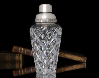 May include: A clear glass cocktail shaker with a silver top and a diamond pattern. The shaker is on a black background.