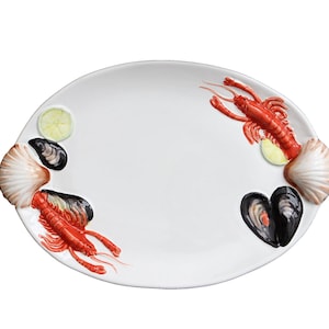 Puede incluir: Plato ovalado blanco con asas de concha, adornado con langostas rojas, mejillones negros y rodajas de limón. Plato decorativo con temática de mariscos para servir.