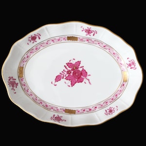 Könnte beinhalten: Eine ovale Servierplatte aus Porzellan mit einem rosafarbenen Blumendesign und goldenen Verzierungen. Die Platte hat einen gewellten Rand und ist perfekt zum Servieren von Snacks oder Vorspeisen.