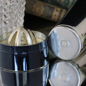 K&ouml;nnte beinhalten: Ein schwarzer Cocktailshaker mit silbernem Deckel und einem silbernen Zitruspresse. Der Shaker tr&auml;gt die Aufschrift "Shake" und "Made in Japan" auf der Unterseite.