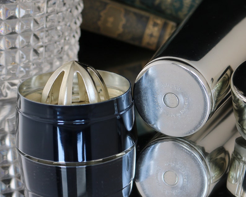 K&ouml;nnte beinhalten: Ein schwarzer Cocktailshaker mit silbernem Deckel und einem silbernen Zitruspresse. Der Shaker tr&auml;gt die Aufschrift "Shake" und "Made in Japan" auf der Unterseite.