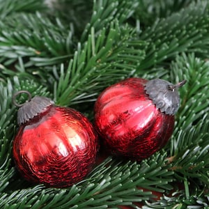 Può includere: Due palline di Natale rosse con cappucci color argento poggiano su un letto di aghi di pino verdi. Gli ornamenti hanno un aspetto strutturato e screpolato, che riflette la luce. Decorazioni natalizie festive.