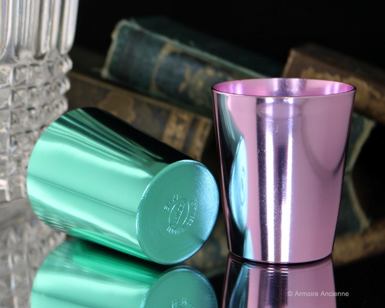 K&ouml;nnte beinhalten: Zwei metallische Becher, einer gr&uuml;n und einer rosa, mit gl&auml;nzender, reflektierender Oberfl&auml;che. Die Becher sind aus Aluminium und haben ein schlichtes, zylindrisches Design.