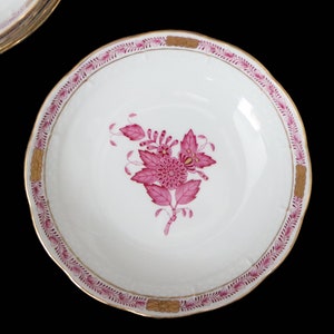 May include: A white porcelain bowl with a pink floral design and a gold rim. The bowl is decorated with a single pink flower and leaves.