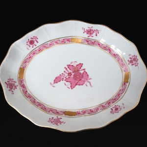 May include: An oval porcelain serving dish with a pink floral design and gold trim. The dish has a scalloped edge and is perfect for serving snacks or appetizers.