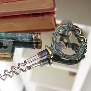 May include: A vintage-style key-shaped bottle opener with a green and gold finish. The opener features a corkscrew and a decorative keyhole design.