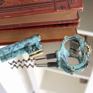 Könnte beinhalten: Ein Vintage-Flaschenöffner- und Korkenzieher-Set in Teal mit goldenen Akzenten. Der Korkenzieher hat eine MetallsSpirale und einen Griff mit einem dekorativen Design. Der Flaschenöffner hat eine einzigartige Form mit einem dekorativen Design.