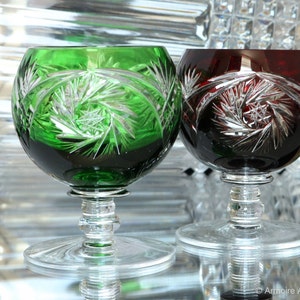 Puede incluir: Dos copas de cristal con tallo y diseños de corte intrincados. Una copa es verde y la otra es roja.