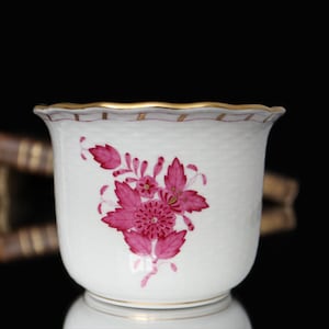 Puede incluir: Una taza de porcelana blanca con un diseño floral rosa y un borde dorado. La taza tiene un borde festoneado y está decorada con un delicado patrón floral.