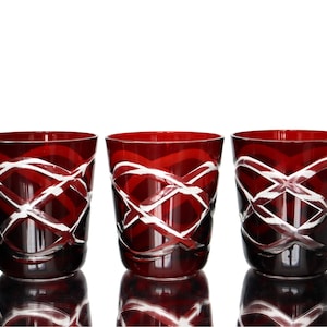 Op de afbeelding: Drie dieprode glazen drinkbekers met een helder, geslepen rasterpatroon dat rond de buitenkant loopt. Elk vat heeft een brede, open rand en een gladde, afgeronde basis, met een levendige karmozijnrode tint en contrasterende transparante lijnen.