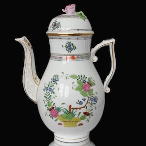 Puede incluir: Cafetera de porcelana blanca con un diseño floral y detalles dorados. La tapa tiene una flor rosa en la parte superior.