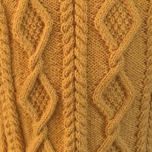 May include: Close-up of a mustard yellow knitted fabric with a cable knit design. The pattern features diamond shapes and vertical braided columns, creating a textured surface. The knitwear showcases a detailed, warm, and cosy aesthetic.