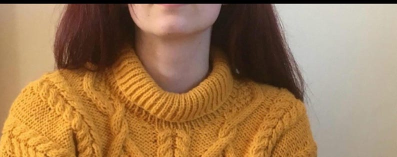 May include: Mustard yellow cable-knit sweater with a ribbed turtleneck. The sweater has a textured pattern across the chest and sleeves. The model is wearing the sweater.