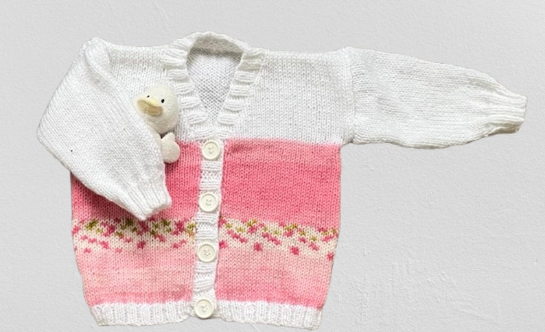 May include: A long-sleeved knit cardigan featuring a white upper section and a pink lower section with a small floral pattern. The garment has a V-neckline, a white button-down front with four white buttons, and ribbed cuffs and hem.