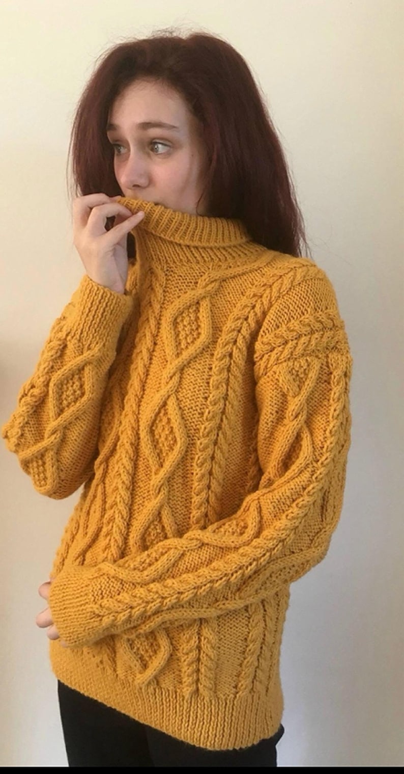 May include: Mustard yellow cable-knit jumper with a roll neck. The jumper features a diamond and braid pattern. The sleeves and body have a textured design. The garment is made of a thick, warm material, perfect for cold weather.