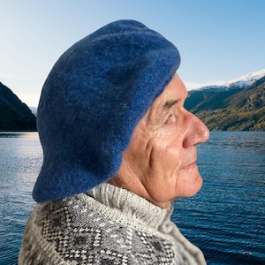 Peut inclure: Un béret en laine feutrée bleu uni avec une calotte arrondie et un bord légèrement évasé. Le chapeau présente une surface dense et texturée ainsi qu'une couleur bleue profonde et saturée. Le design est simple, avec une construction lisse.