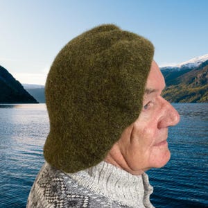 May include: A solid olive green felted wool hat with a rounded crown and a short, curved brim. The hat features a dense, textured surface and is worn covering the top of the head, extending down to the ears in a simple, functional design.