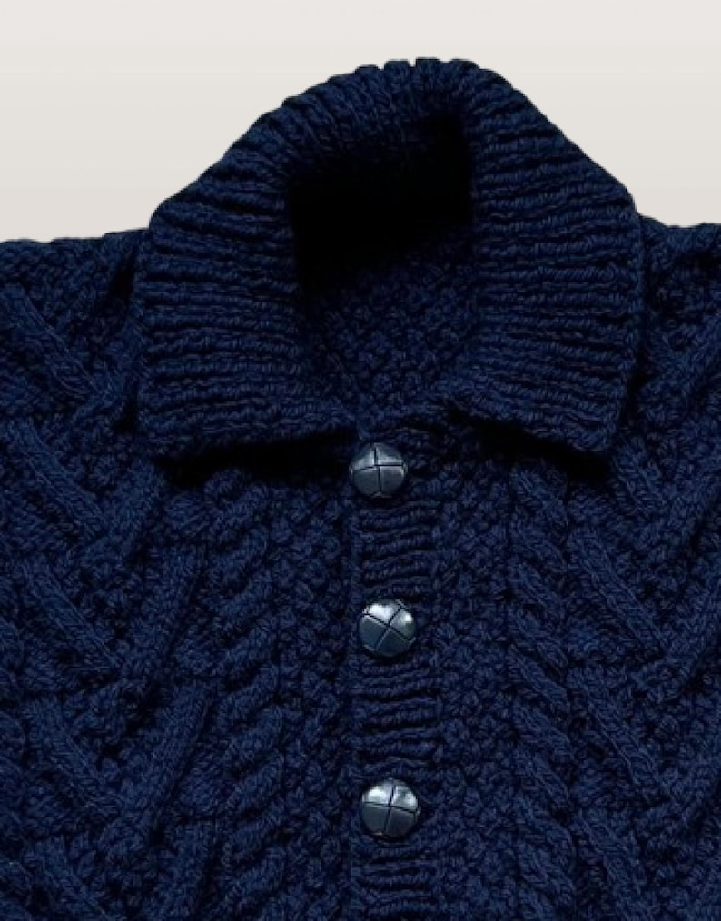 May include: A dark navy blue knit sweater featuring a thick folded collar, a vertical button placket with three round dark buttons, and a textured cable knit pattern throughout the fabric. The garment has a structured neckline and long sleeves.
