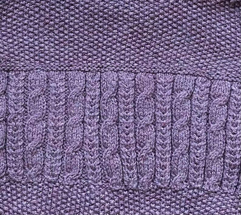 May include: Close-up of a knitted fabric in shades of purple. The top and bottom sections have a textured, tight knit, while the middle section features a cable knit design. The overall texture is soft and detailed.