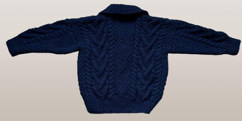 May include: A dark navy blue long-sleeve sweater featuring a prominent cable knit pattern throughout the body and sleeves. The garment includes a wide fold-over collar and ribbed cuffs at the wrists and hem, showcasing a thick, textured knit construction.