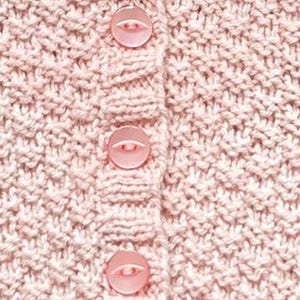 Op de afbeelding: Close-up van een lichtroze gebreid vest met drie bijpassende knopen. Het breipatroon is getextureerd en de knopen hebben een lichtere roze tint. Het vest lijkt gemaakt van een zacht, mogelijk wollen materiaal.