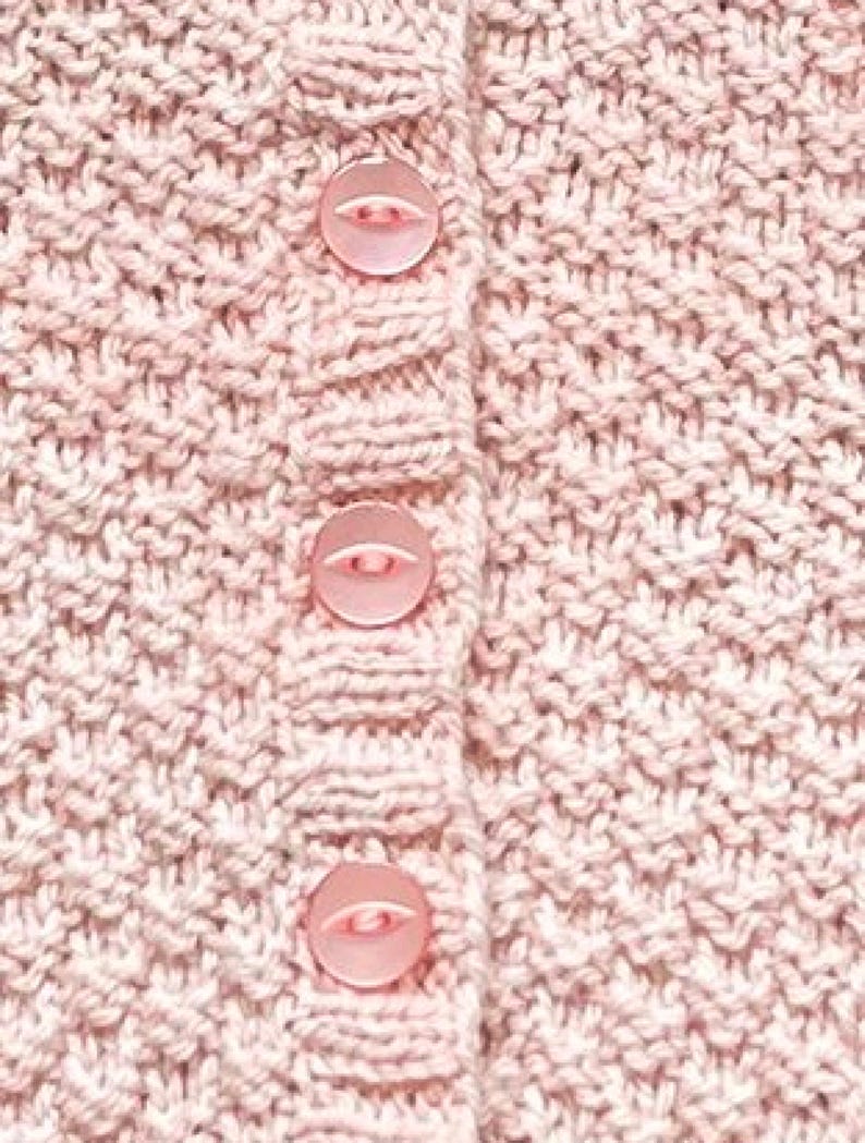Op de afbeelding: Close-up van een lichtroze gebreid vest met drie bijpassende knopen. Het breipatroon is getextureerd en de knopen hebben een lichtere roze tint. Het vest lijkt gemaakt van een zacht, mogelijk wollen materiaal.