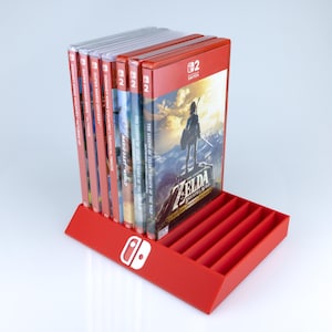 May include: A red Nintendo Switch game cartridge holder with a white Nintendo logo. The holder is filled with game cases, including "The Legend of Zelda: Breath of the Wild". The holder has multiple slots for game storage.