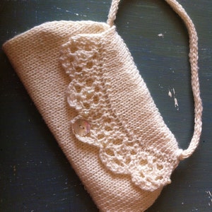 May include: A white crocheted clutch bag with a decorative lace trim and a single button closure.