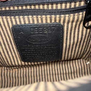 May include: The interior of a handbag featuring a black leather patch embossed with the Brighton logo and the serial number 095997. The lining consists of a beige and black vertical striped fabric. The text on the patch describes the collection.
