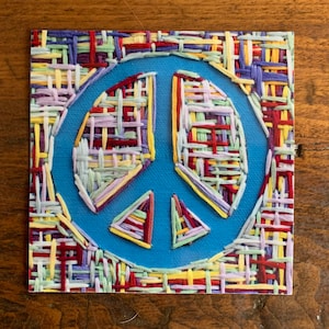 May include: A blue peace sign with a colorful woven pattern around the edges.