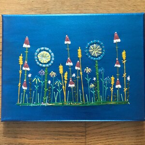 May include: A blue canvas painting with an embroidered design of a field of flowers. The flowers are white, red, yellow, and blue. The background is a deep blue.