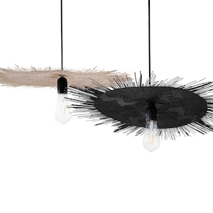 May include: Two pendant lights with a circular, spiky design. One is beige, the other black. Each has a black fixture and a visible lightbulb. The lights hang from black cords against a white background.
