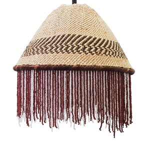May include: A woven lampshade with a brown and white pattern and a fringe of red and white beads.